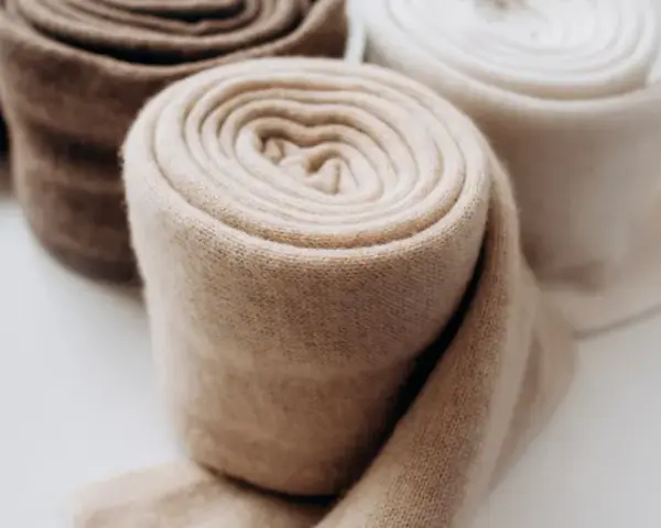 Rotoli di morbido cashmere in tonalità naturali, pronti per il lavaggio e la cura.
