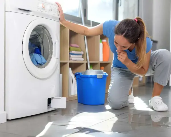 Donna preoccupata guarda la lavatrice che perde acqua e lascia residui di sporco sul pavimento.