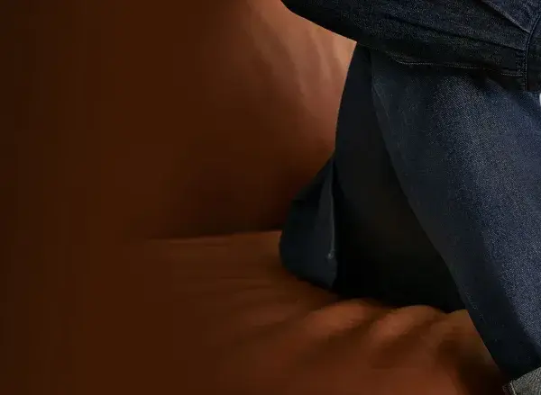 Uomo seduto su un divano di pelle, indossa un completo in denim. Il suo braccio è appoggiato sulla gamba, mostrando la texture del tessuto.