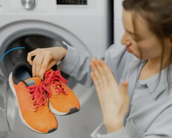 Donna con scarpe arancioni davanti a una lavatrice. Scopri come fare un lavaggio a vuoto per pulire la lavatrice.