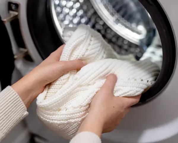 Mani che inseriscono un maglione bianco nella lavatrice, sperando che la lavatrice non lava bene i bianchi.
