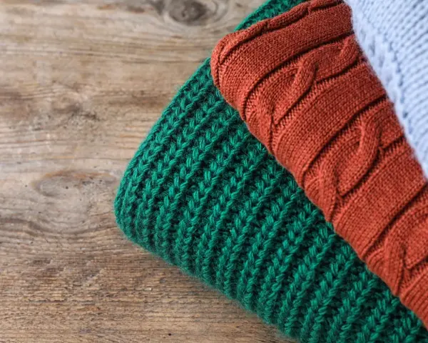 Close-up of folded knitted wool in green, rust, and light blue on a wooden surface.