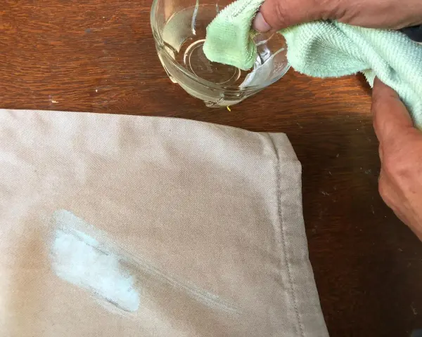 Mani che tamponano macchie di colore su tessuto con un panno umido.