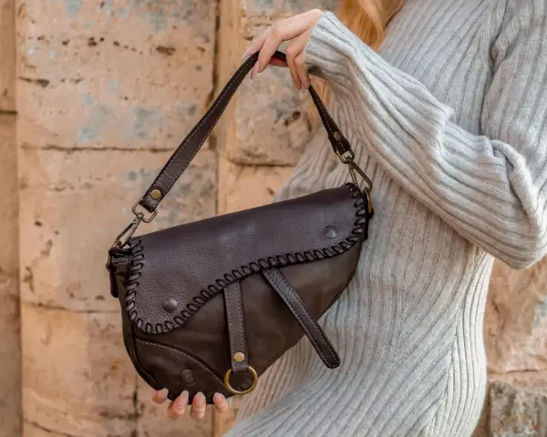 Donna con borsa a tracolla in pelle marrone, con cuciture decorative. Scopri come ammorbidire la pelle delle borse per un look sempre perfetto.
