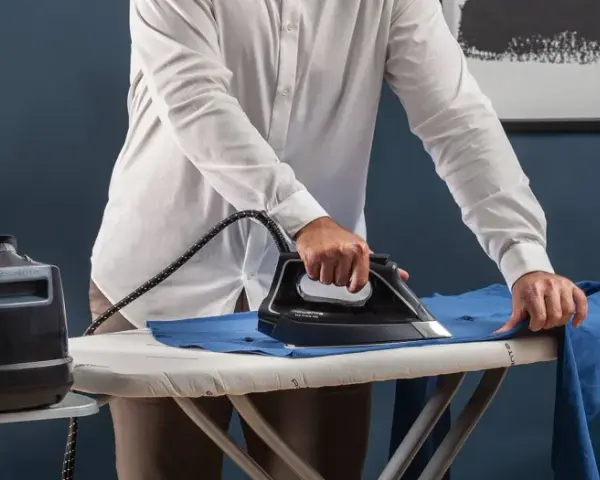Uomo stira una camicia blu su un asse da stiro. Impara come stirare il poliestere con cura per risultati impeccabili.