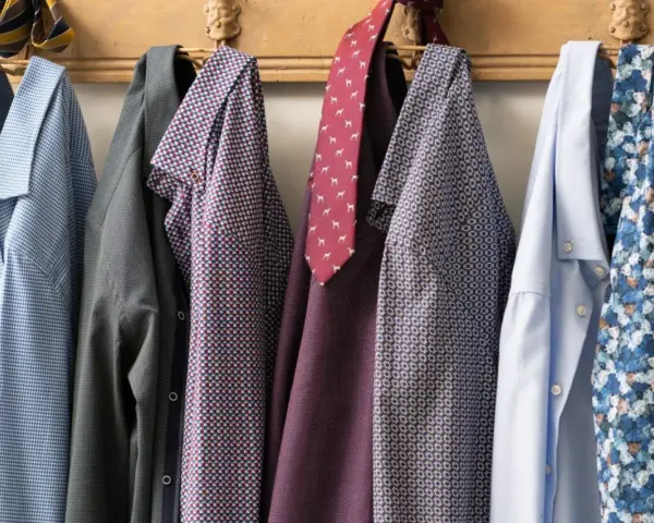 Camicie da uomo con fantasie diverse appese a un attaccapanni. Un promemoria su come lavare le camicie a mano per mantenerle perfette.