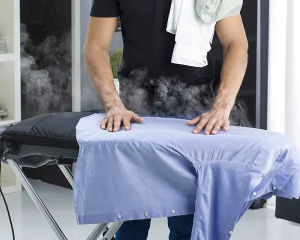 Uomo stira camicia azzurra con vapore. Per un lavaggio misto in lavatrice, quanti gradi?