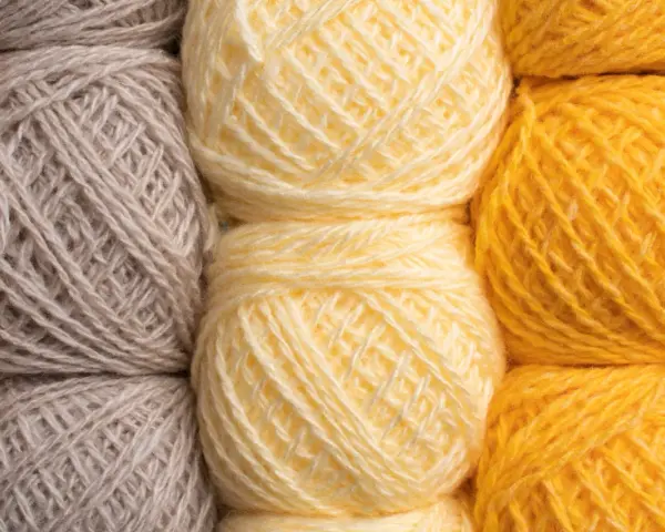 Gomitoli di lana in tonalità naturali: grigio, giallo tenue e giallo vivace. Diversi tipi di lana pronti per creare maglie calde.