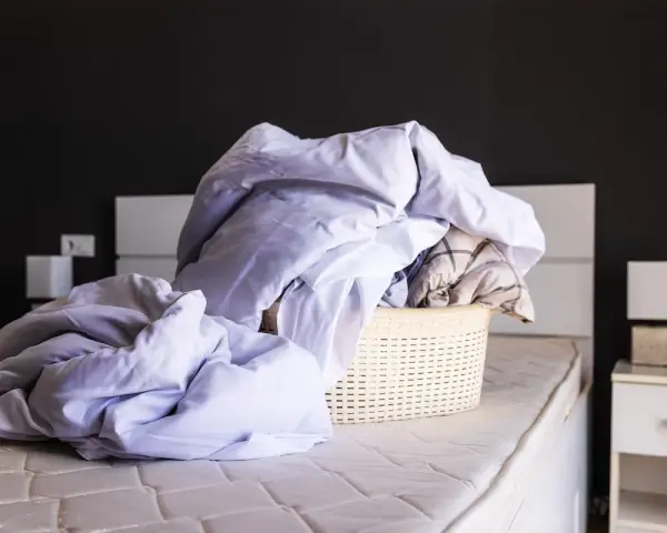 Cesto di biancheria da letto accartocciata, pronto per il bucato. Un promemoria per imparare come smacchiare il lino e far brillare le lenzuola.