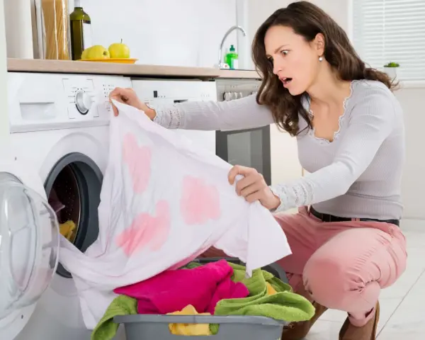 Donna sorpresa scopre una maglietta bianca macchiata di rosa, tipici errori di bucato causati dalla dispersione del colore.