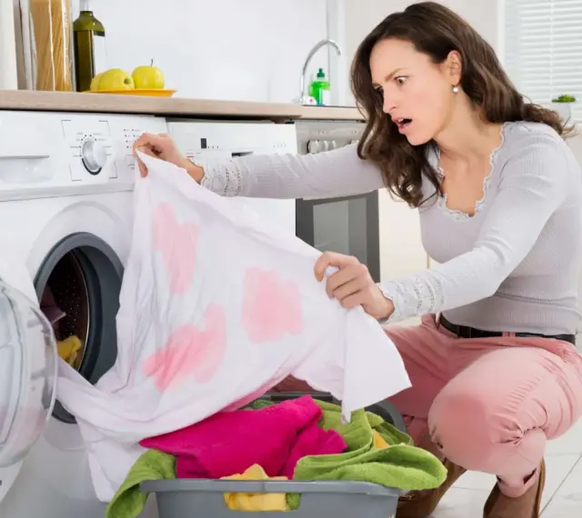 Donna sorpresa scopre una maglietta bianca macchiata di rosa, tipici errori di bucato causati dalla dispersione del colore.