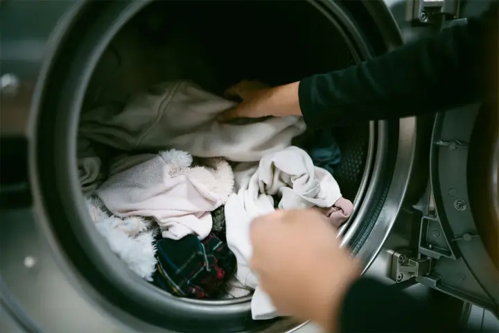 Mani che caricano la lavatrice con panni chiari, sperando di non trovare macchie bianche sui vestiti dopo lavatrice.