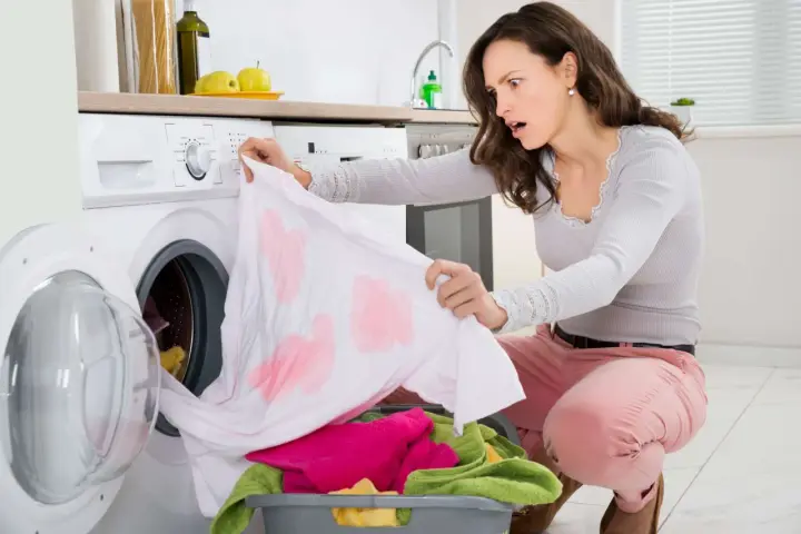 Donna sorpresa scopre una maglietta bianca macchiata di rosa, tipici errori di bucato causati dalla dispersione del colore.
