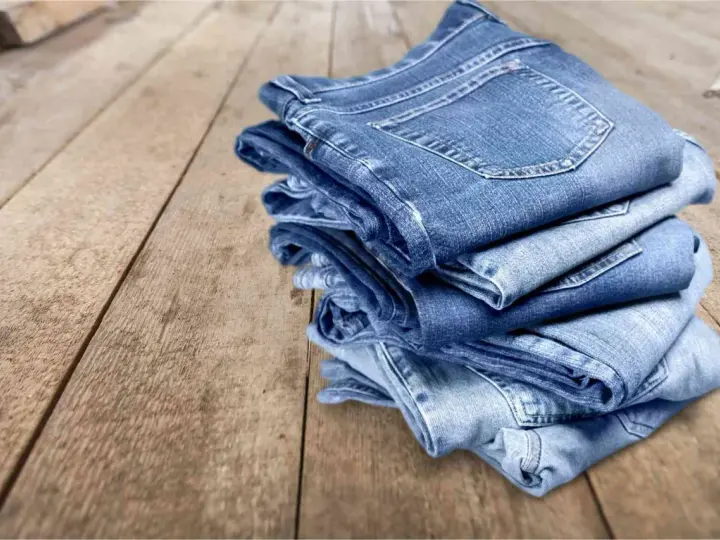 Pile di jeans su un tavolo di legno. Scopri come evitare che i jeans perdano colore.