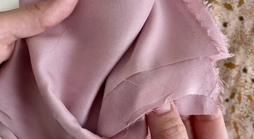 Mani che accarezzano un tessuto di viscosa rosa cipria, mostrando come lavare la viscosa a mano per preservarne la morbidezza.