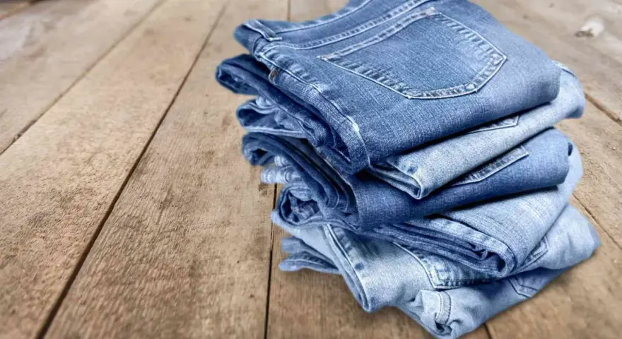 Pile di jeans su un tavolo di legno. Scopri come evitare che i jeans perdano colore.