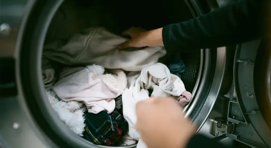 Mani che caricano la lavatrice con panni chiari, sperando di non trovare macchie bianche sui vestiti dopo lavatrice.