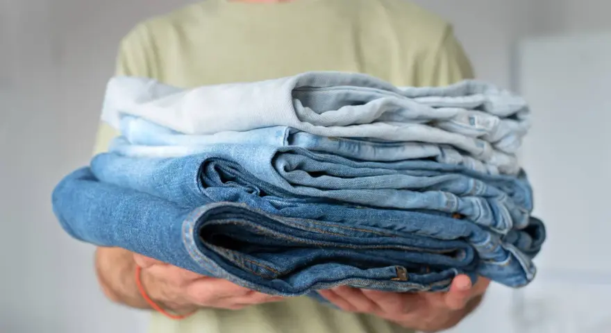 Un uomo tiene una pila di jeans duri dopo lavaggio, con tonalità di blu che vanno dal chiaro allo scuro.