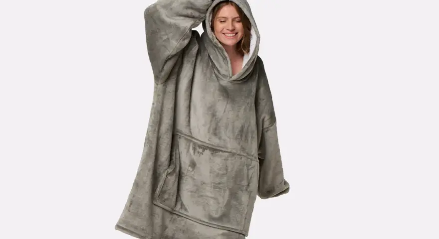 Donna sorridente indossa una coperta con cappuccio grigia, realizzata in poliestere, un materiale sintetico caldo e confortevole.