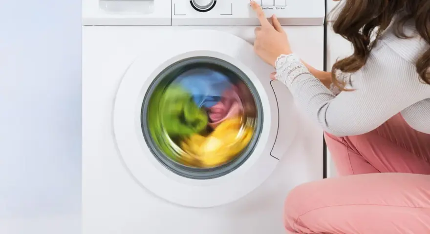 Donna preme il pulsante per avviare la lavatrice. Il cestello gira velocemente, mostrando i panni colorati in movimento.