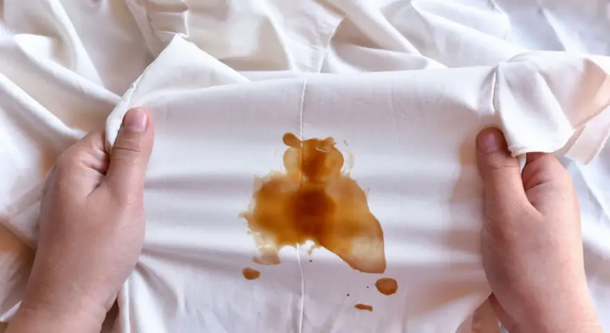 Mani che tengono un vestito bianco macchiato di caffè, forse caduto da una borsa in pelle.