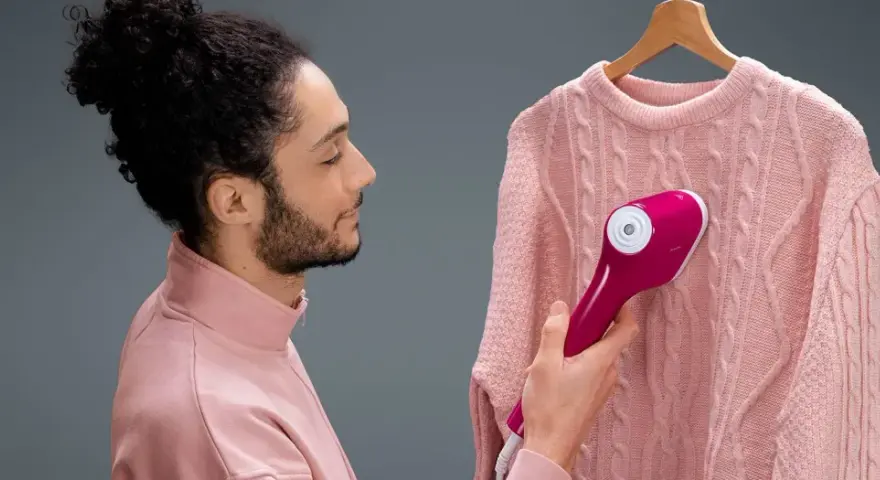 Uomo con maglione rosa usa un ferro da stiro verticale che non emette vapore, sperando di eliminare le pieghe.
