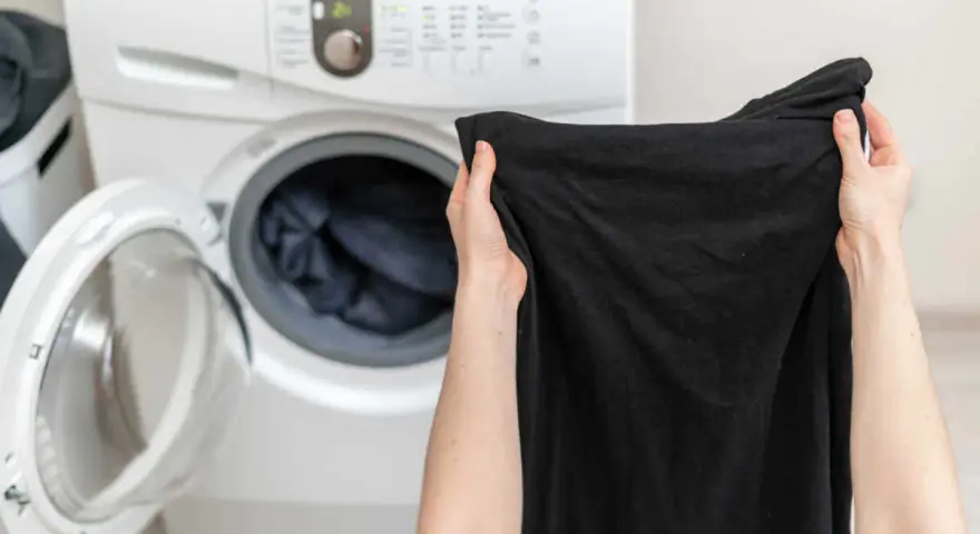 Mani che tengono capi neri, pronti per essere messi nella lavatrice aperta.