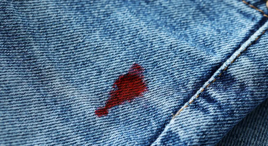 Macchia rossa su jeans blu. Attenzione, l'acqua ossigenata macchia i vestiti, lasciando segni indelebili.