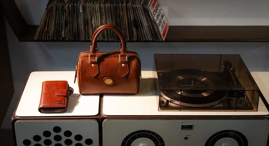 Borsa in pelle marrone, portafoglio e giradischi vintage. Un set per chi ama la musica e lo stile classico, pronto per essere pulito.