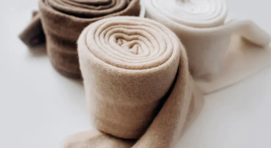 Rotoli di morbido cashmere in tonalità naturali, pronti per il lavaggio e la cura.
