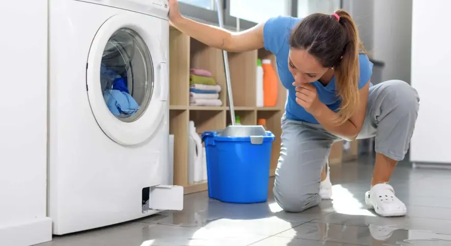 Donna preoccupata guarda la lavatrice che perde acqua e lascia residui di sporco sul pavimento.