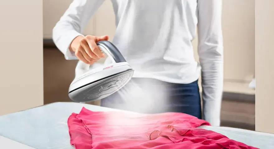 Donna stira un abito rosa con il ferro da stiro Polti Kalstop, creando vapore.