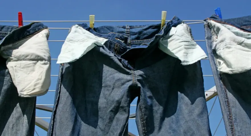 Pantaloni in denim appesi ad asciugare al sole, con tasche interne visibili.
