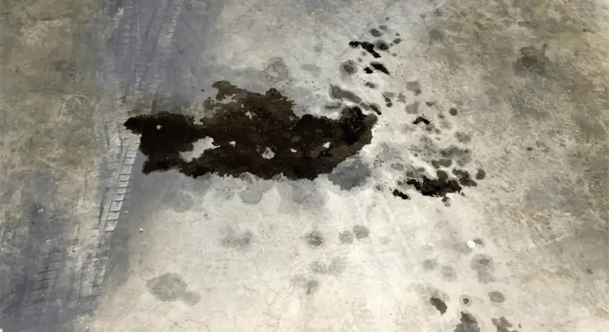 Macchie scure di grasso meccanico su cemento, con impronte di pneumatici. Un problema comune da risolvere per chi vuole togliere macchie di grasso meccanico.