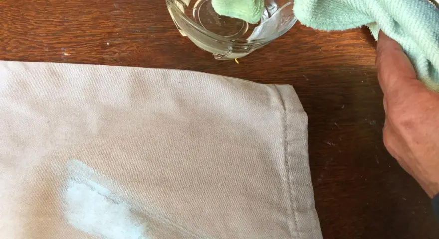 Mani che tamponano macchie di colore su tessuto con un panno umido.