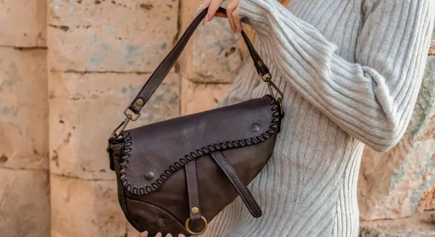 Donna con borsa a tracolla in pelle marrone, con cuciture decorative. Scopri come ammorbidire la pelle delle borse per un look sempre perfetto.