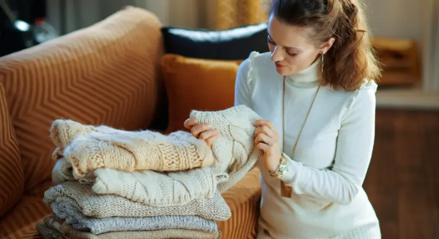 Donna esamina una pila di maglioni di lana, pensando a come togliere i pallini dalle maglie di lana per mantenerli perfetti.