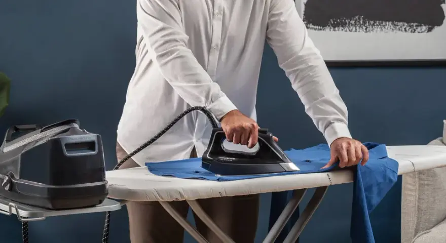 Uomo stira una camicia blu su un asse da stiro. Impara come stirare il poliestere con cura per risultati impeccabili.