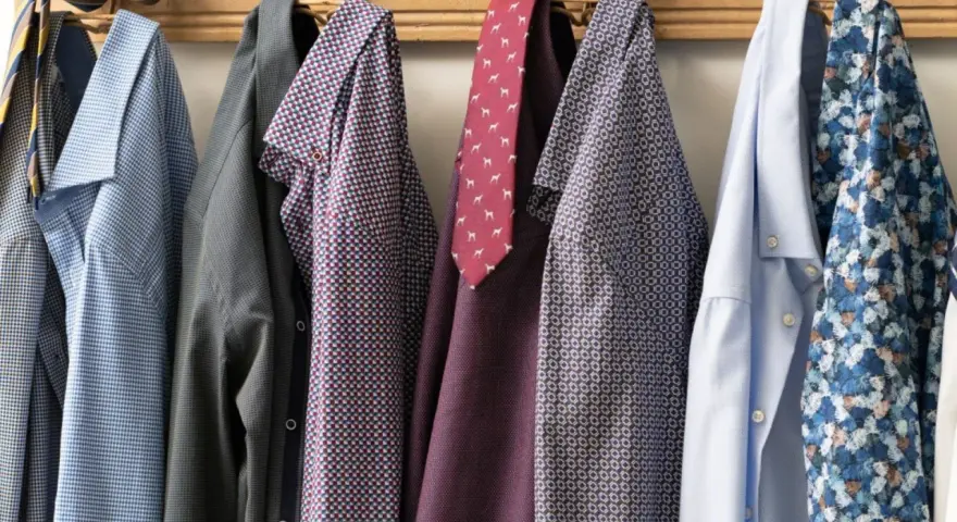Camicie da uomo con fantasie diverse appese a un attaccapanni. Un promemoria su come lavare le camicie a mano per mantenerle perfette.