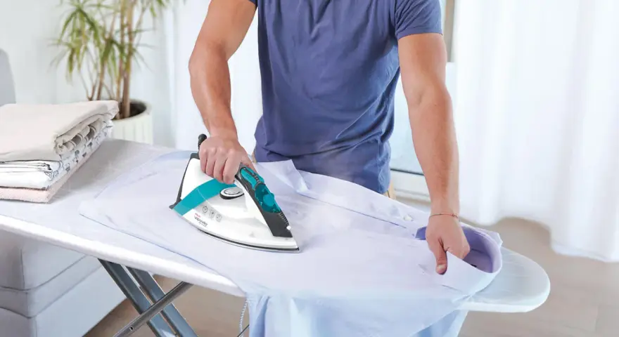 Uomo stira una camicia. Impara come pulire la piastra del ferro da stiro per risultati perfetti.