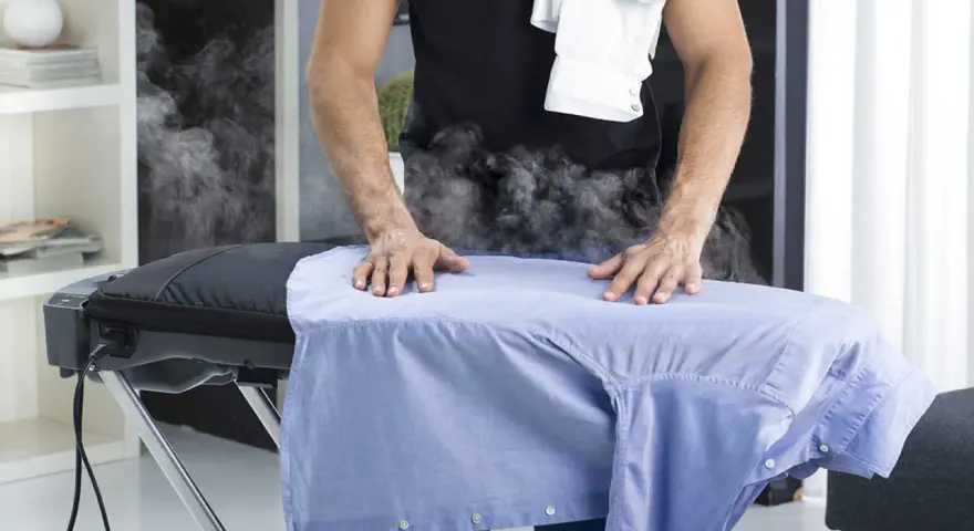 Uomo stira camicia azzurra con vapore. Per un lavaggio misto in lavatrice, quanti gradi?