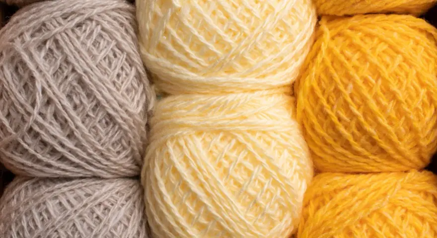 Gomitoli di lana in tonalità naturali: grigio, giallo tenue e giallo vivace. Diversi tipi di lana pronti per creare maglie calde.