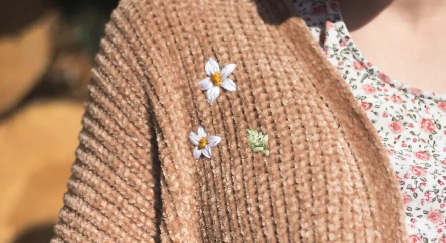 Delicati ricami su maglioni di lana: due fiorellini bianchi e una fogliolina verde aggiungono un tocco di natura a un caldo cardigan color caramello.