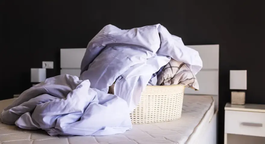 Cesto di biancheria da letto accartocciata, pronto per il bucato. Un promemoria per imparare come smacchiare il lino e far brillare le lenzuola.