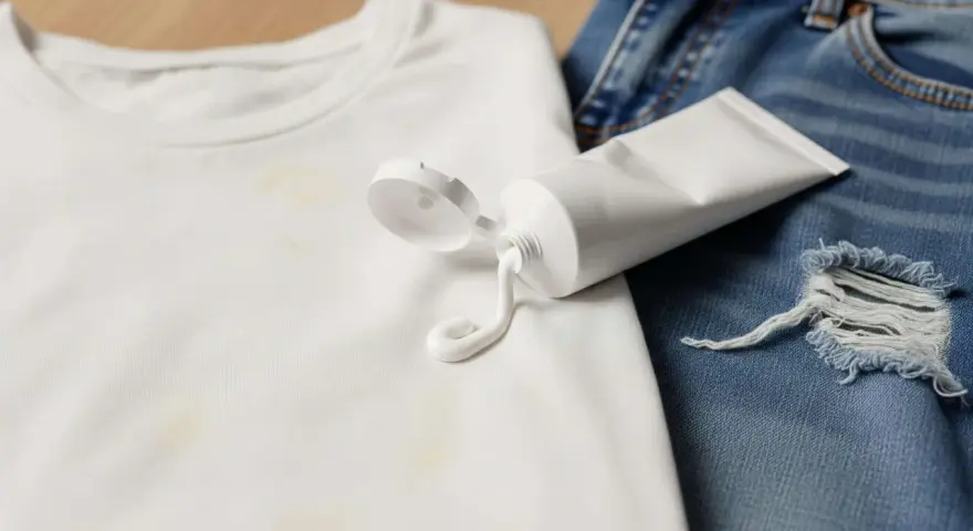 Tubo di crema sbiancante su maglietta bianca macchiata e jeans strappati. Scopri trucchi per togliere le macchie di candeggina.