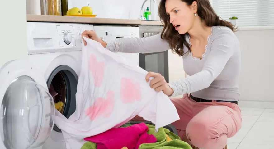 Donna sorpresa scopre una maglietta bianca macchiata di rosa, tipici errori di bucato causati dalla dispersione del colore.