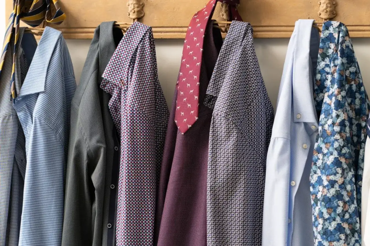 Camicie da uomo con diverse fantasie e cravatte appese a un attaccapanni. Una guida su come lavare le camicie a mano.