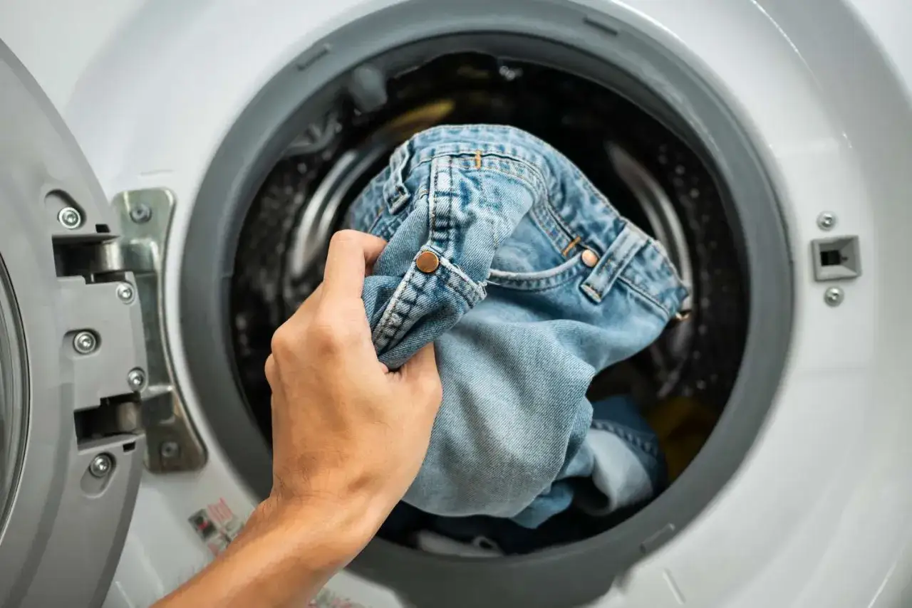 Mano inserisce jeans chiari nella lavatrice. Ecco come lavare i jeans in lavatrice per mantenerli come nuovi.