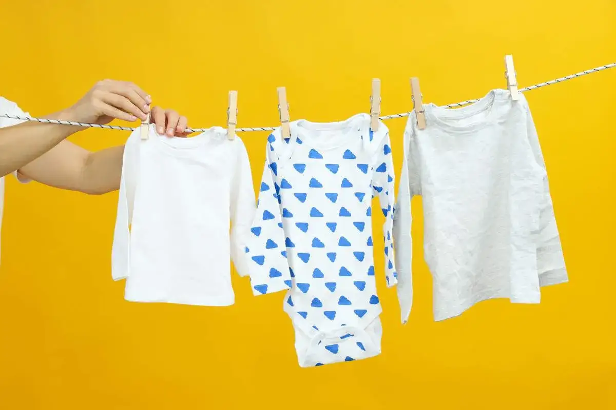 A mano appende vestiti per bambini su uno stendibiancheria. Il modal tessuto puzza, ma questi sono puliti e pronti per essere indossati.