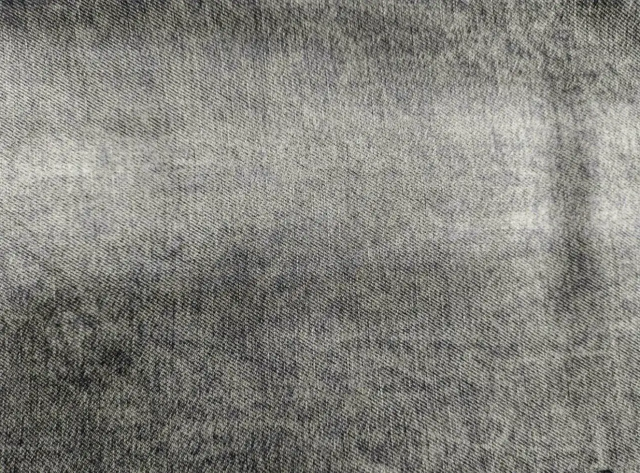Texture di denim grigio chiaro con sfumature pi&ugrave; scure, che ricorda un tessuto vissuto e morbido.